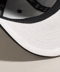 Limited first edition 'A' cap, a classic snapback by Uppr Lowr. The cap features a hand-drawn custom letterform 'A' by Travis Price, exclusive for Uppr Lowr. Crafted from a wool blend, it showcases custom raised embroidery and a deep fit. This collectable cap is a must-have for streetwear enthusiasts.